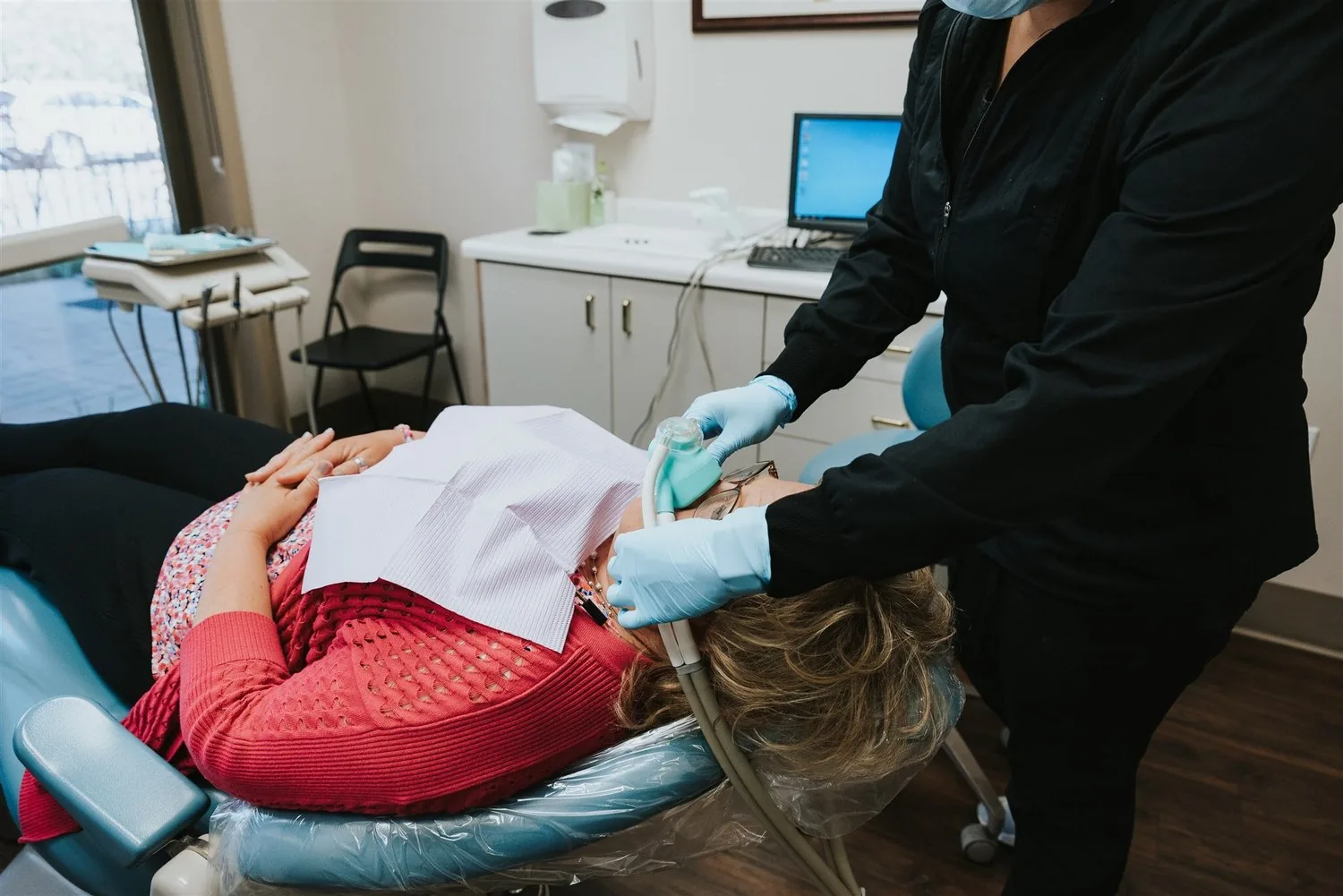 A dental professional placing a nitrous oxide mask on a patient reclining in a dental chair.